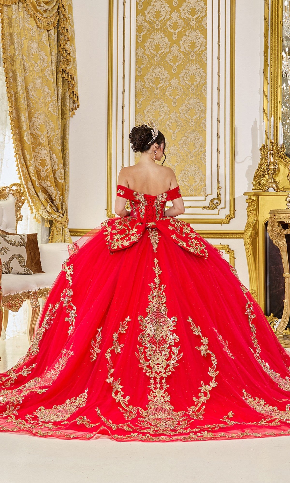 A woman wearing the Quinceanera Dress 5086 By Dancing Queen, featuring red fabric, gold embroidery, and a lace-up corset, stands with her back to the camera in an ornate gold-decorated room.